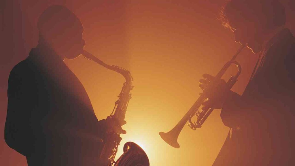 Zwei Musiker spielen Saxophon und Trompete vor einem orangefarbenen Licht.