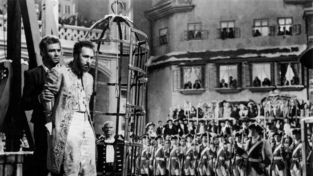 Szene aus dem Film 'Jud Süß' mit einem Mann in einem Käfig und einem anderen Mann, der ihn festhält.