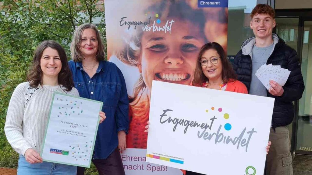 Vier Personen halten Plakate und Auszeichnungen für den Jugendförderpreis 2023 in einem Innenraum.