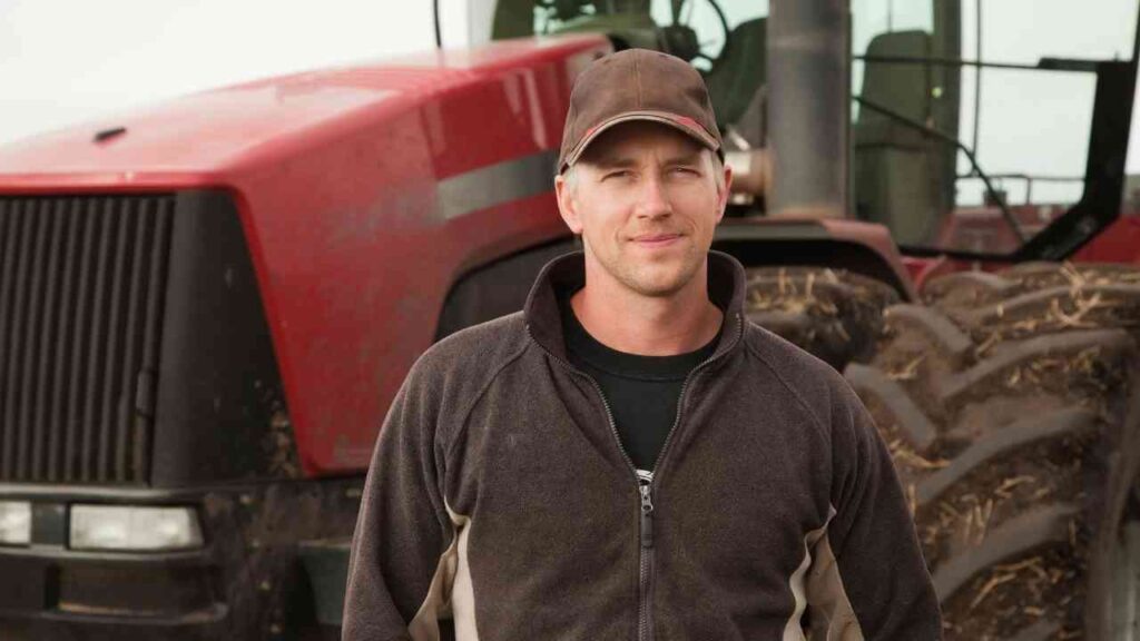 Ein Landwirt steht vor einem roten Traktor auf einem Feld.