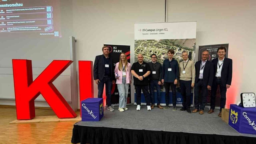 Gruppe von Personen steht auf einer Bühne vor einem großen roten KI-Schild bei einer Veranstaltung in Lingen.