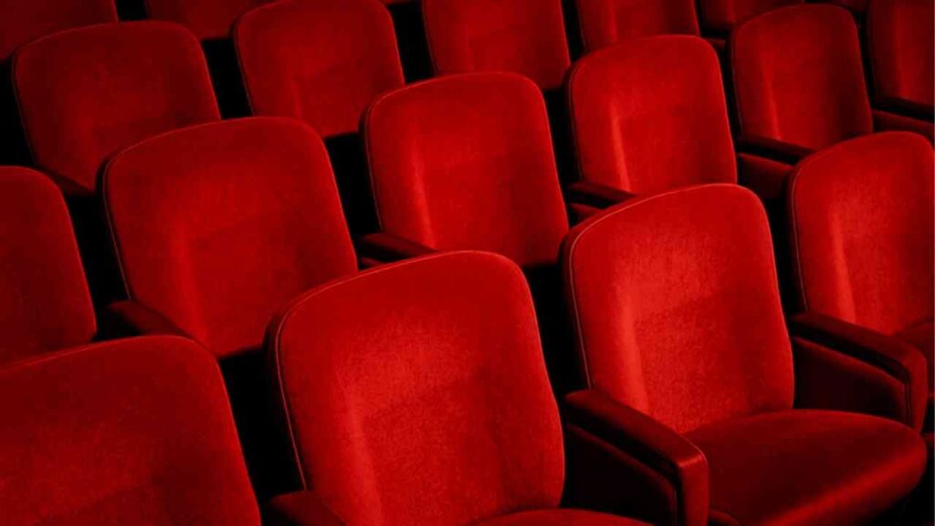 Reihen von roten, gepolsterten Kinosesseln in einem dunklen Raum, die für eine Kinovorführung angeordnet sind.