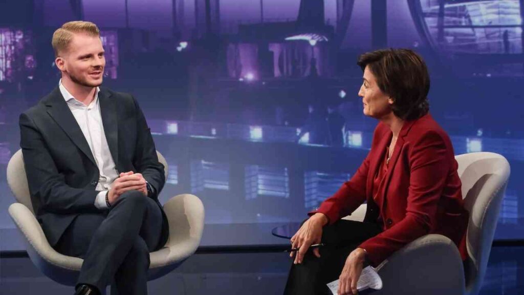 Zwei Personen in einem Studio während eines Interviews, eine sitzt und die andere spricht.