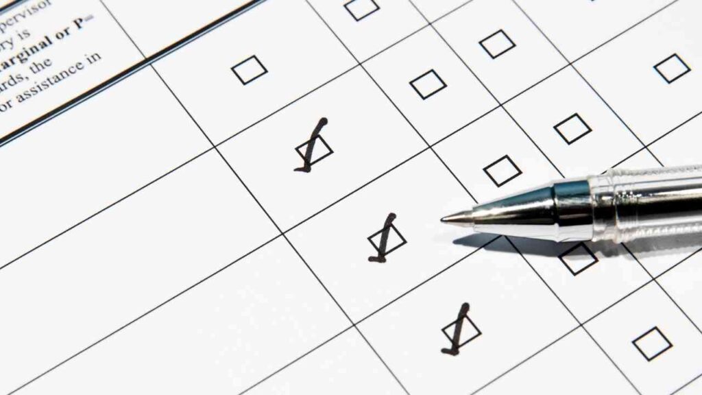 Papier mit Kästchen und Häkchen, daneben ein silberner Kugelschreiber.