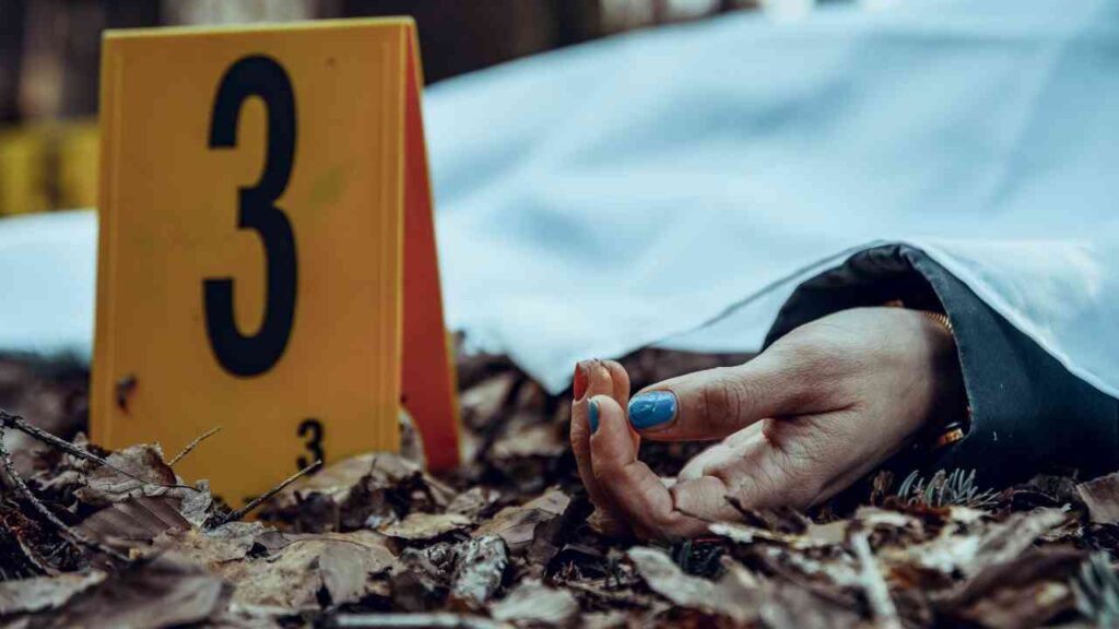 Eine Hand mit blauen Nägeln liegt unter einem weißen Tuch, neben einem gelben Beweisstück mit der Nummer 3.