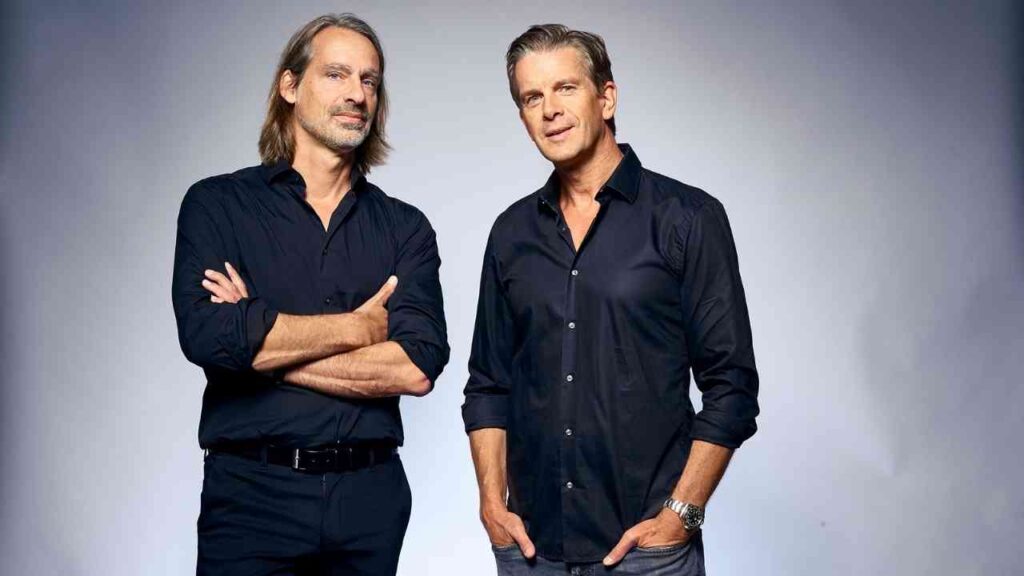 Zwei Männer in schwarzen Hemden stehen nebeneinander und posieren für ein Porträtfoto.