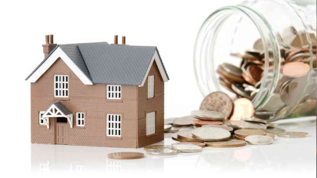 Modell eines Hauses neben einem Glas mit Münzen, das auf einem Tisch steht.