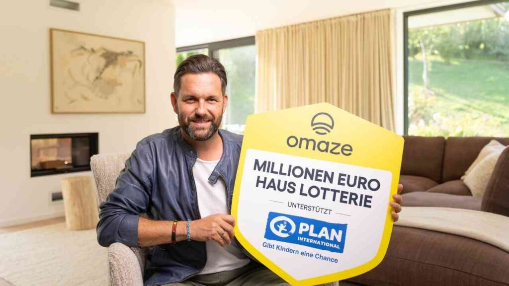 Mann hält ein Schild mit der Aufschrift 'Millionen Euro Hauslotterie' und dem Logo von Plan International.