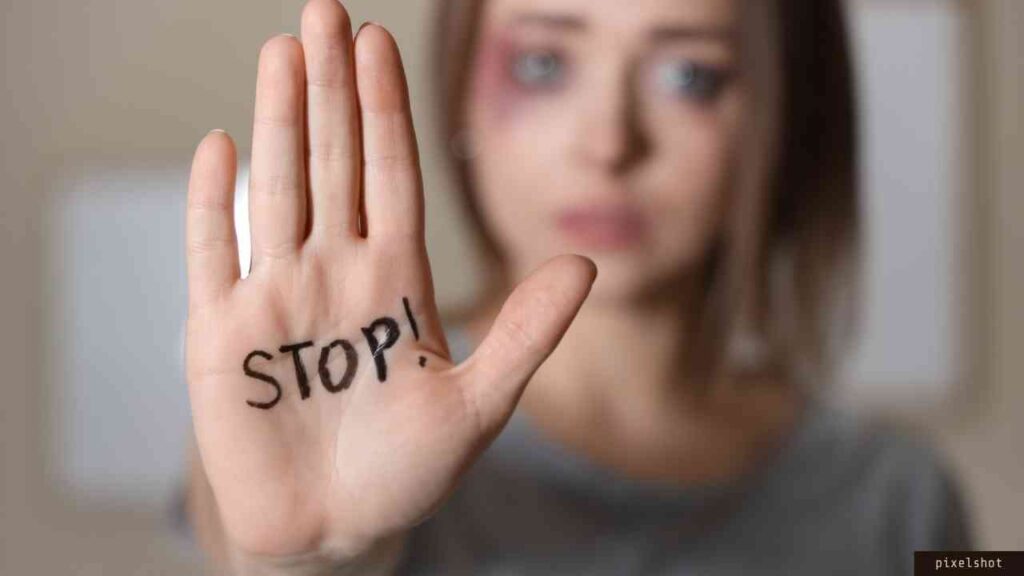 Eine Frau mit einer verletzten Gesichtshaut hält ihre Hand mit der Aufschrift 'STOP!' in die Kamera.