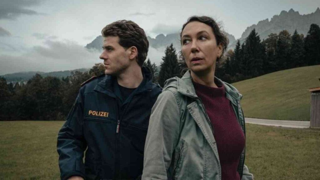 Zwei Personen in einer ländlichen Landschaft, Polizistenszene vor bewaldeten Hügeln und Bergen im Hintergrund.