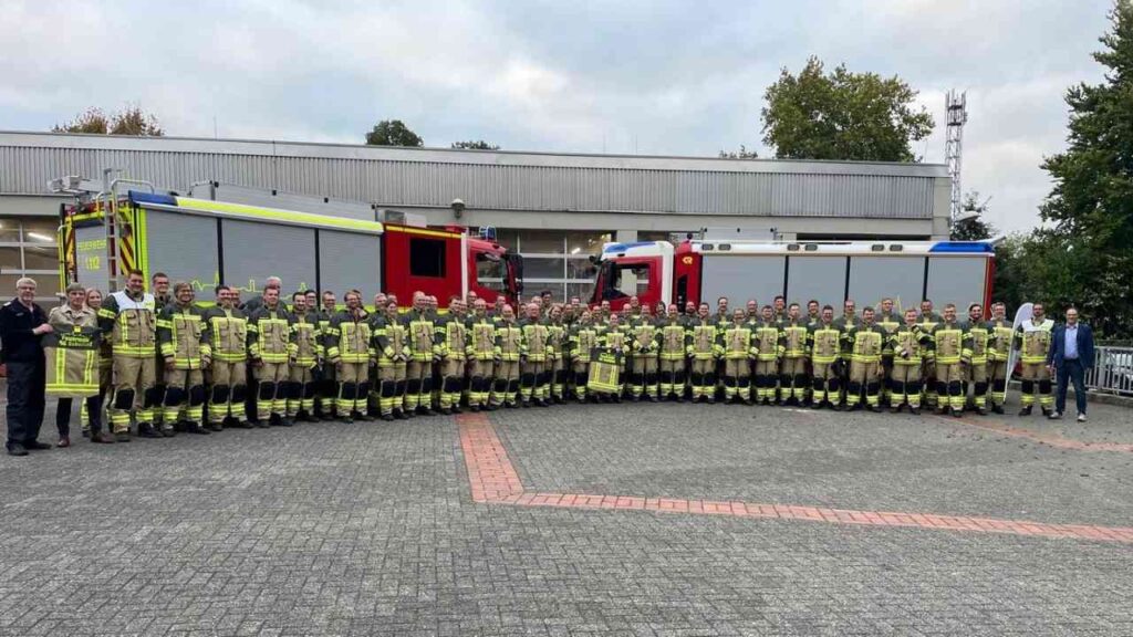Gruppe von Feuerwehrleuten in Schutzanzügen vor Einsatzfahrzeugen, bereit für den Einsatz, Gruppenbild, Feuerwehrstation.