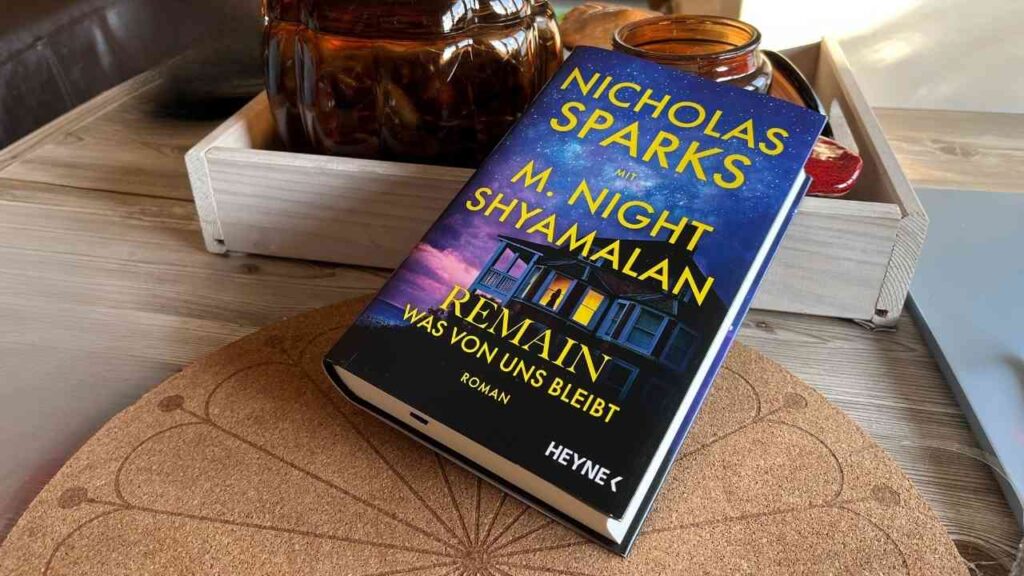 Buchcover von 'Remain' von Nicholas Sparks und M. Night Shyamalan auf einem Tisch.