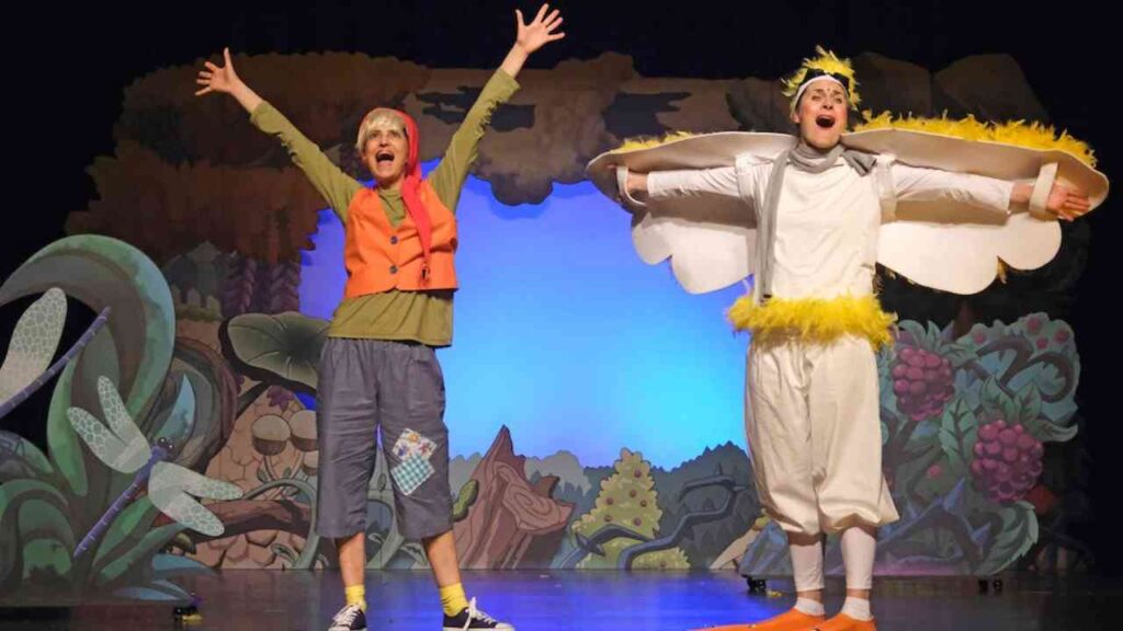 Zwei Schauspieler in bunten Kostümen auf einer Bühne während einer Theateraufführung.