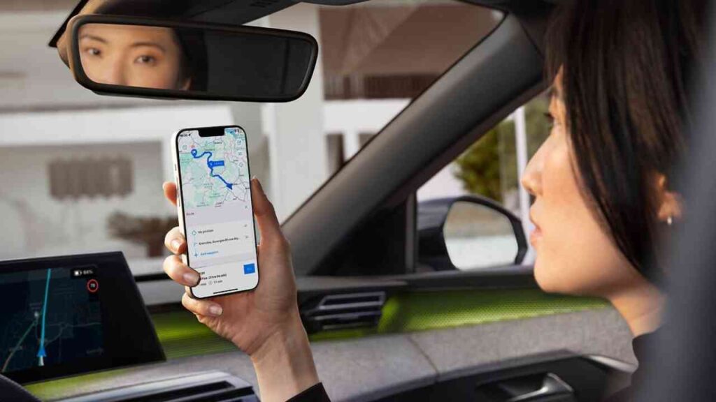 Frau im Auto hält ein Smartphone mit einer Navigationskarte in der Hand, während sie in den Rückspiegel schaut.