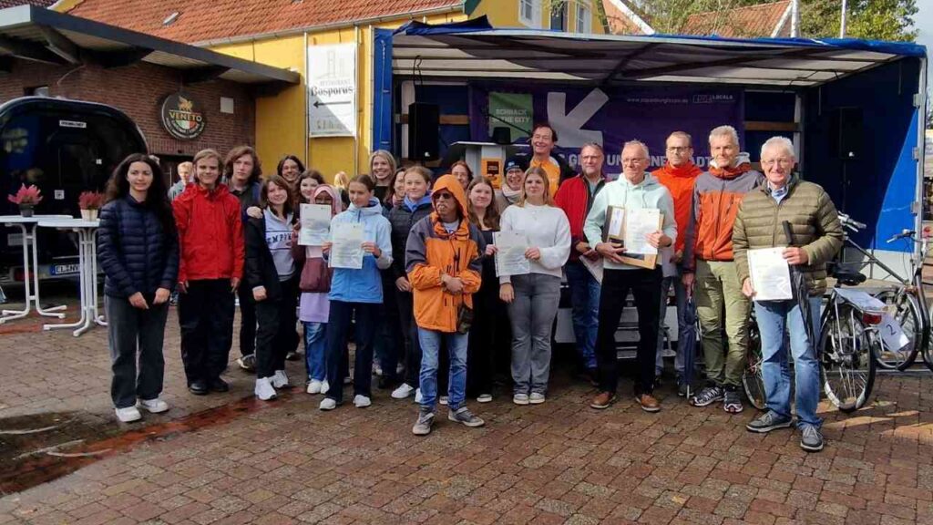 Gruppenfoto von Personen, die Urkunden in einer Stadt präsentieren.