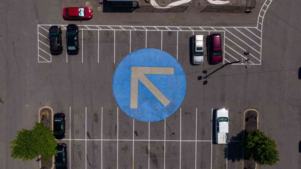 Überblick über einen Parkplatz mit einem blauen Richtungspfeil auf dem Boden und mehreren geparkten Autos.