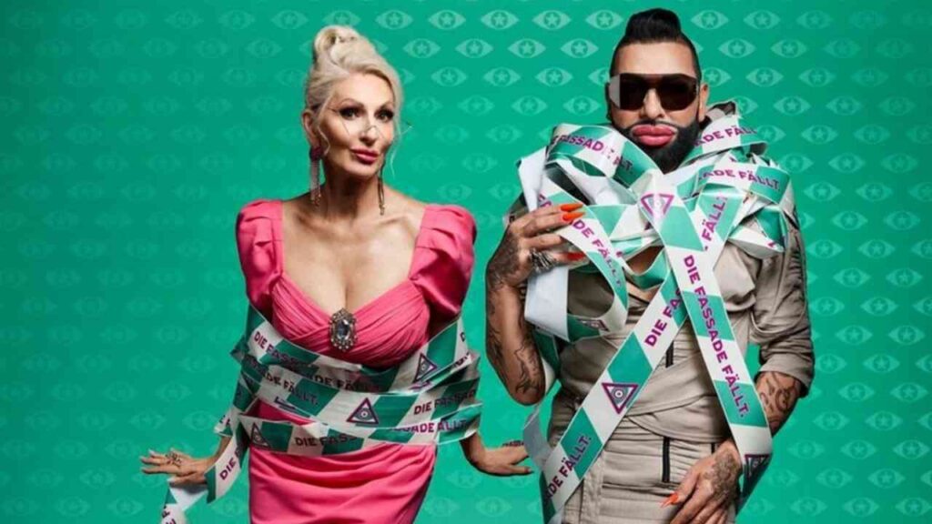 Zwei Personen in auffälligen Outfits, umwickelt mit buntem Absperrband, vor einem grünen Hintergrund.