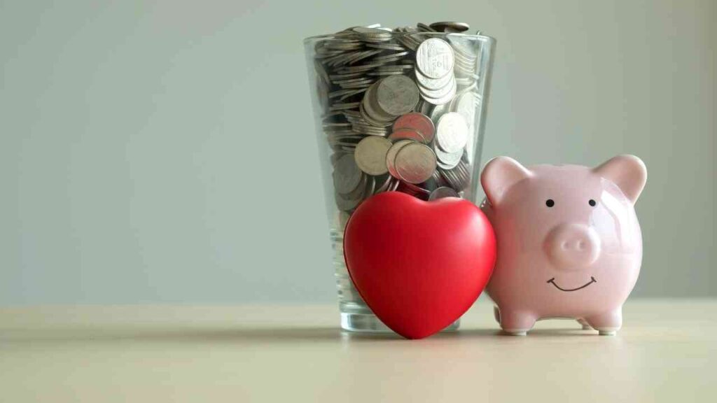 Ein Glas mit Münzen und ein rotes Herz neben einem Sparschwein in Form eines Schweins.