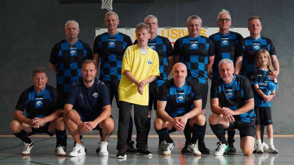 SCP07 posiert in blauen Trikots mit Kind und Trainer, indoor in einer Sporthalle.