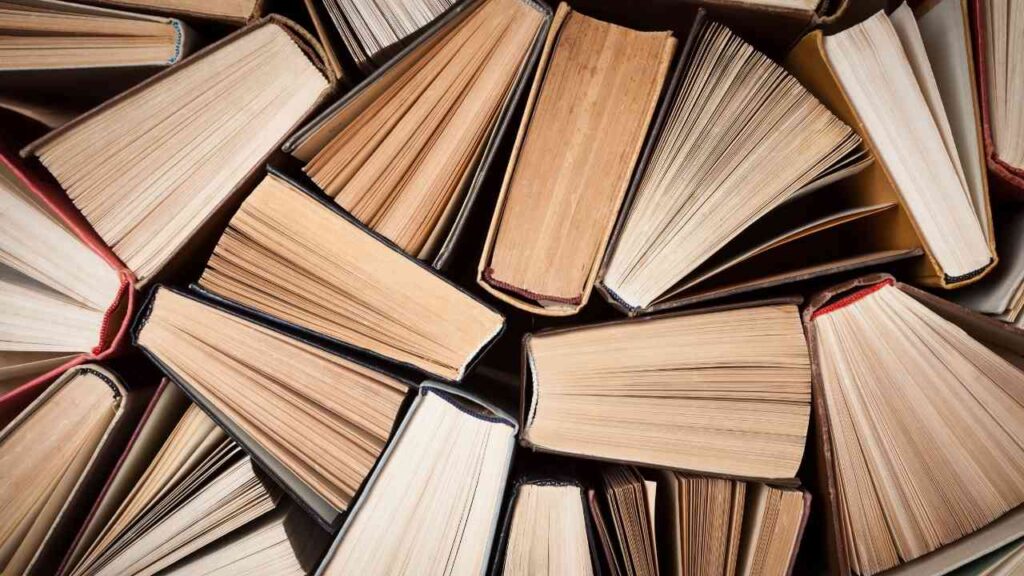 Stapel von offenen und geschlossenen Büchern in verschiedenen Größen und Farben auf einem Tisch.