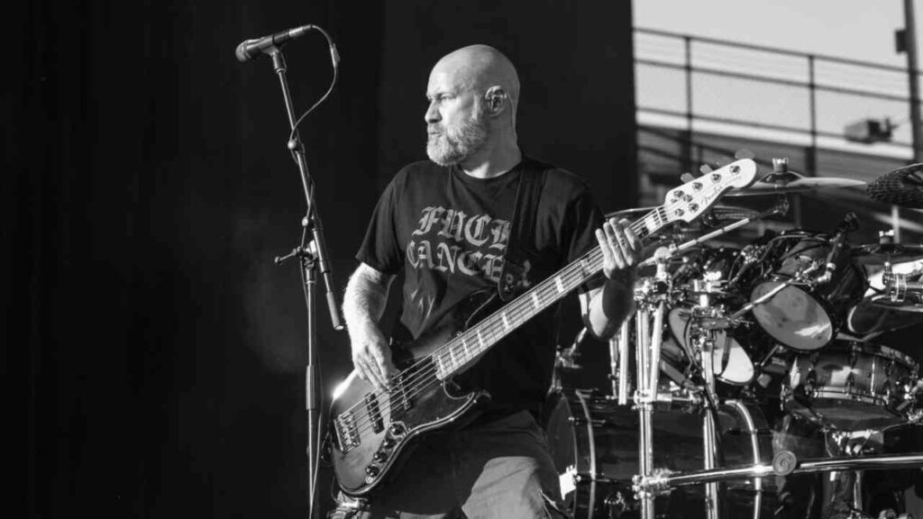 Bassist auf der Bühne, der ein schwarzes T-Shirt mit der Aufschrift 'FUCK CANCER' trägt und ein E-Bass spielt.