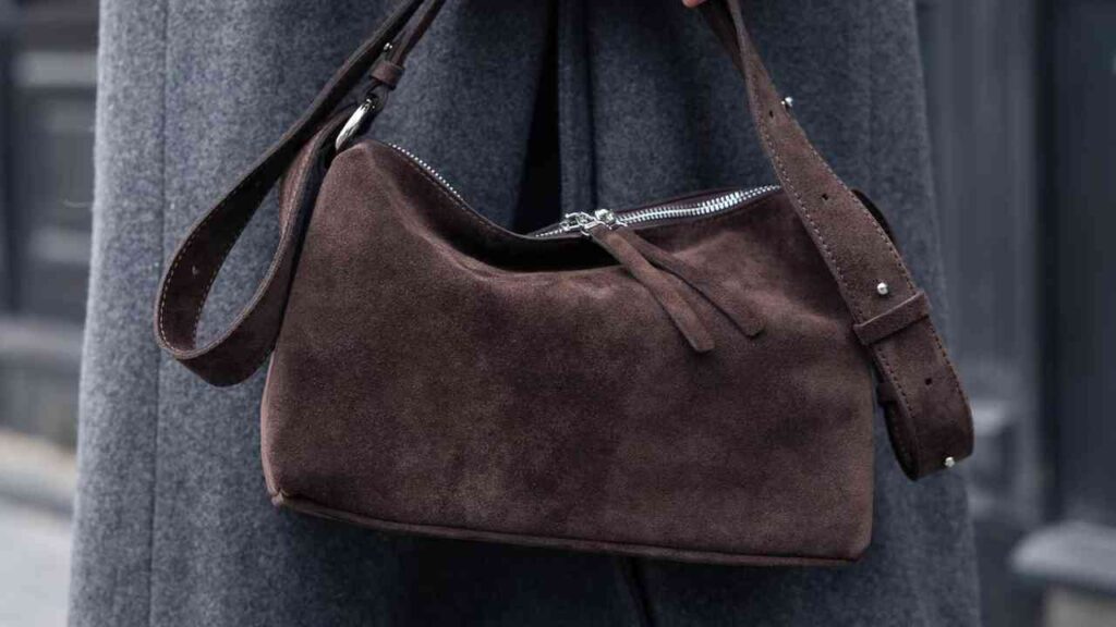 Schokoladenbraune Wildledertasche mit Reißverschluss und verstellbarem Schulterriemen.