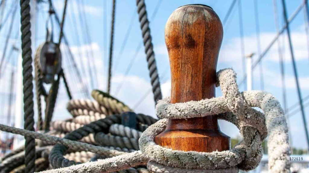 Holzpoller mit Seil auf einem Schiff, umgeben von weiteren Seilen und Takelage.