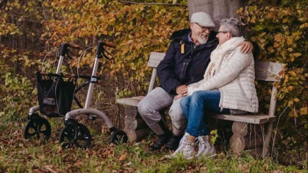 Älteres Paar sitzt auf einer Bank im Freien, während ein Rollator neben ihnen steht.