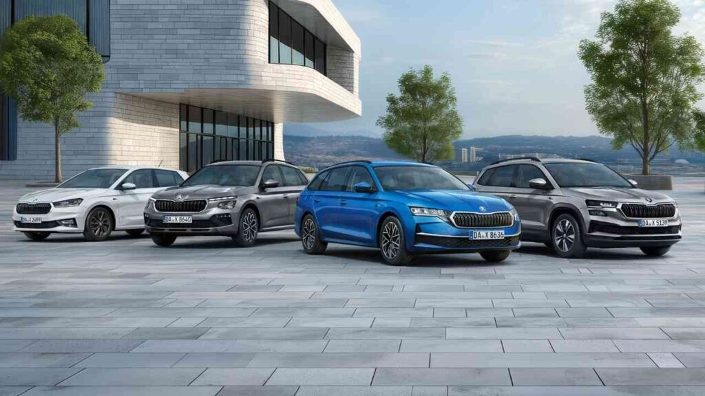 Vier Škoda Fahrzeuge in verschiedenen Farben auf einem modernen Platz angeordnet, darunter ein weißes, graues, blaues und schwarzes Modell.