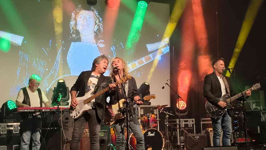 Spirit of Smokie performt auf Bühne mit Gitarren und Keyboard, bunte Lichter erzeugen lebhafte Konzertatmosphäre.