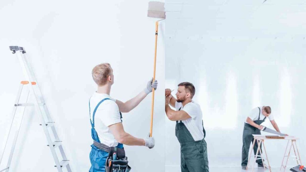 Drei Handwerker, die in einem Raum Wände streichen und Möbel montieren.