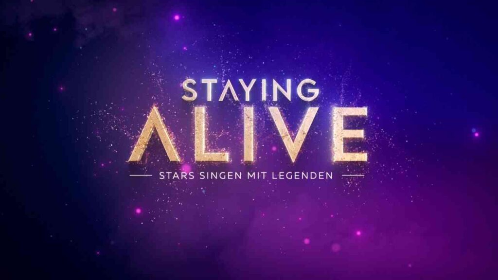 Logo von 'Staying Alive - Stars Singen mit Legenden' in goldenen Buchstaben auf lila Hintergrund.