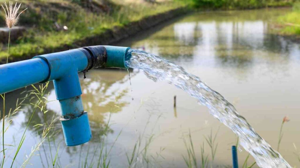 Blauer Wasserrohr, das Wasser in einen Teich leitet, umgeben von Gras und Pflanzen.