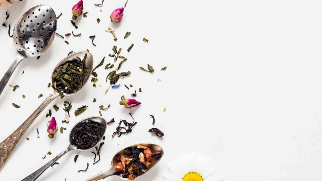 Verschiedene Teesorten in Löffeln, darunter grüner Tee, schwarzer Tee und Kräutertee.