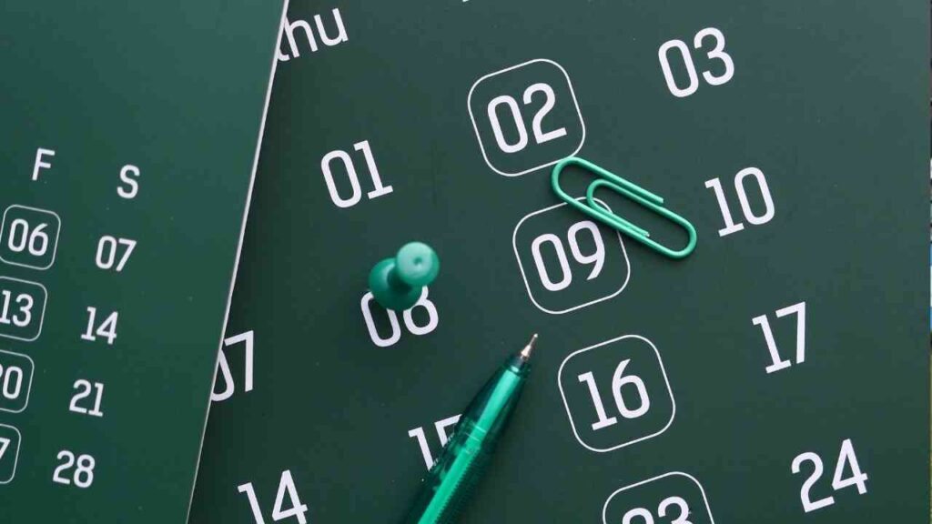 Grüner Kalender mit Datumsangaben, Büroklammer und Stift auf einem Tisch.