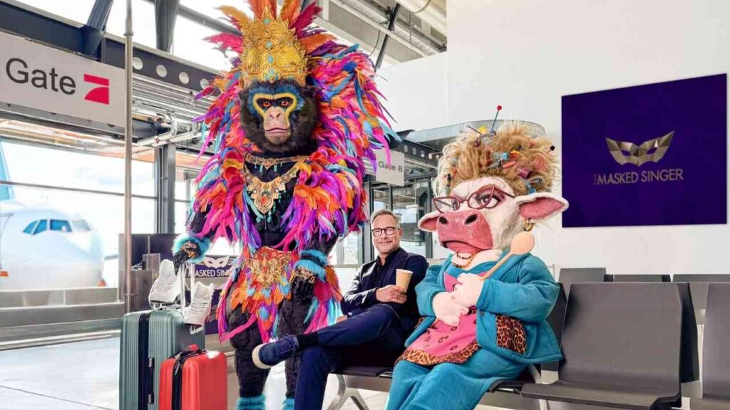 Bunt kostümierte Figuren am Flughafen, eine mit einem farbenfrohen Affenkostüm und die andere in einem rosa Outfit mit Brille.