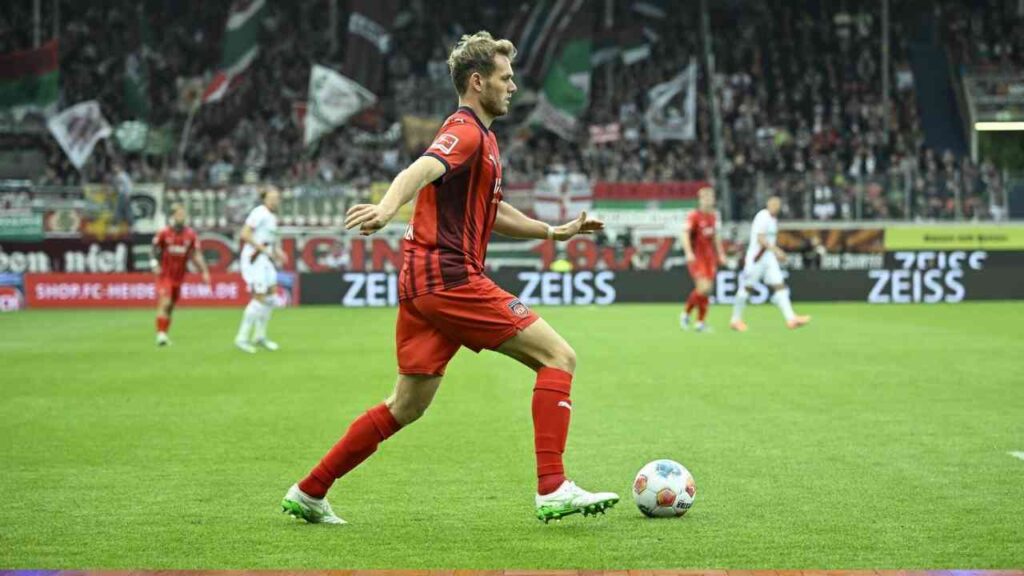 Fußballspieler in rotem Trikot mit Ball auf dem Spielfeld während eines Spiels in der Bundesliga.