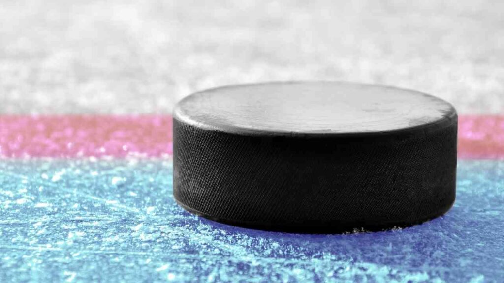 Schwarzer Eishockey-Puck auf einer gefrorenen Eisfläche mit bunten Linien im Hintergrund.
