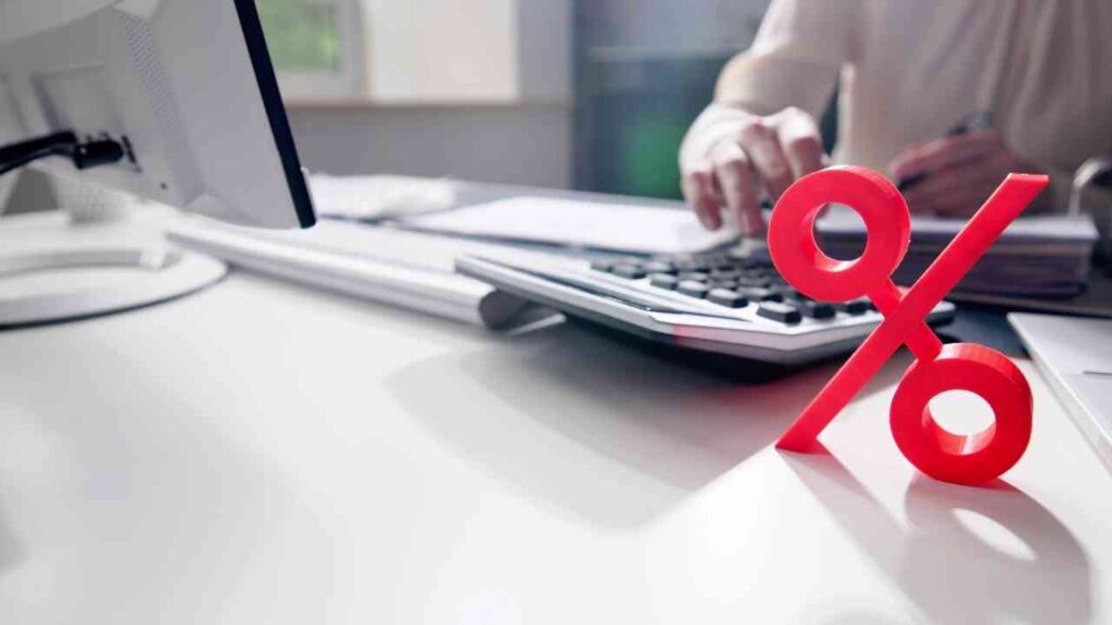 Rote Prozentzeichen-Dekoration auf einem Schreibtisch neben einem Taschenrechner und einem Computer.