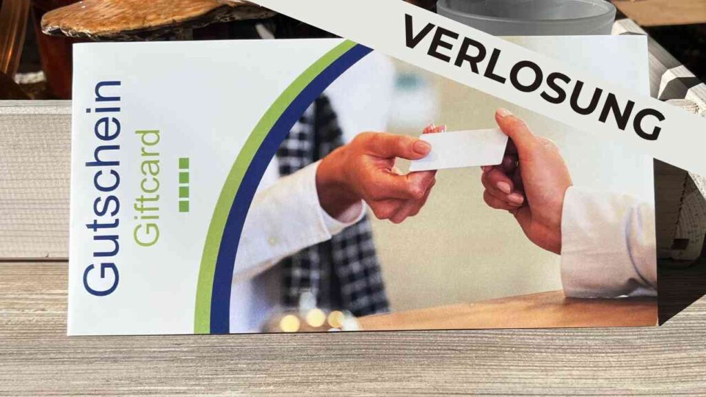 Gutschein mit der Aufschrift 'Verlosung', der von einer Hand an eine andere übergeben wird.