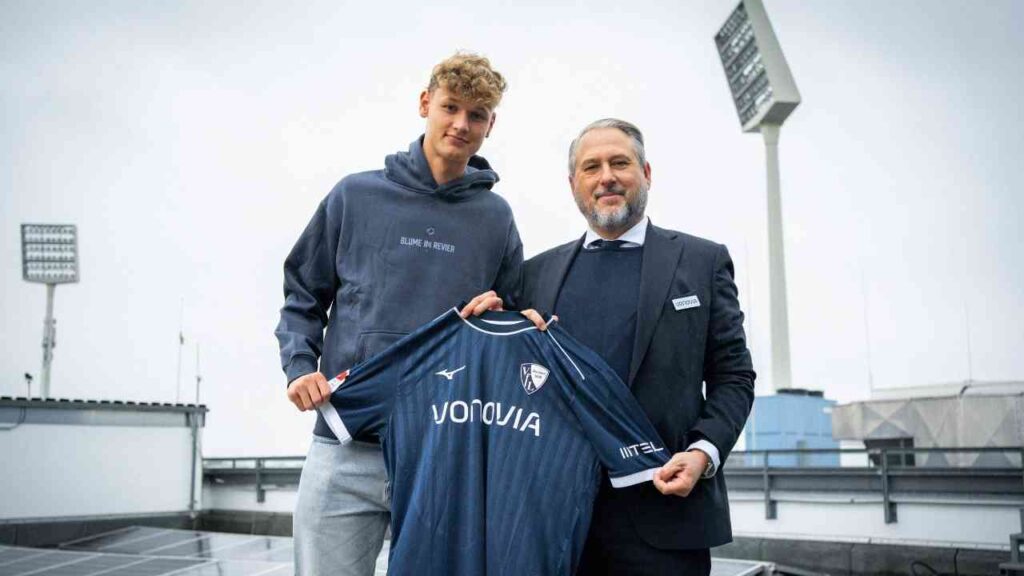 Tom Meyer hält ein VfL Bochum Trikot in der Hand, während er neben einem Vereinsvertreter steht.