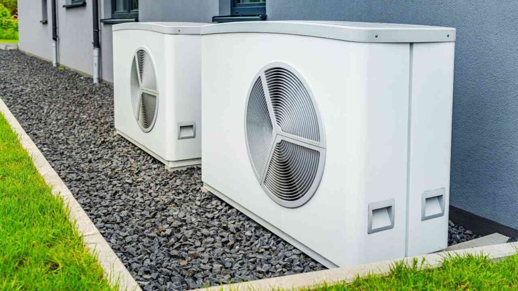 Zwei weiße Wärmepumpen nebeneinander auf einem Kiesbett neben einem Gebäude installiert.