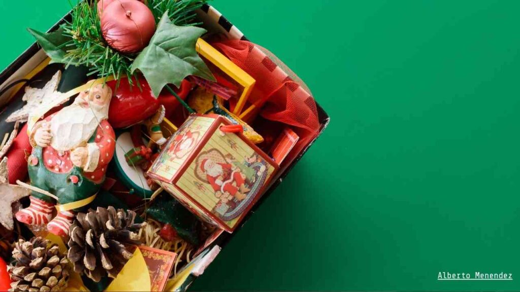 Bunter Schuhkarton gefüllt mit Weihnachtsdekoration, darunter Figuren, Geschenke und Tannenzapfen.