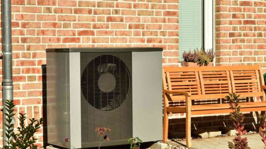 Wärmepumpe in einem modernen Design, platziert an einer Ziegelwand neben einer Holzbank und Pflanzen.