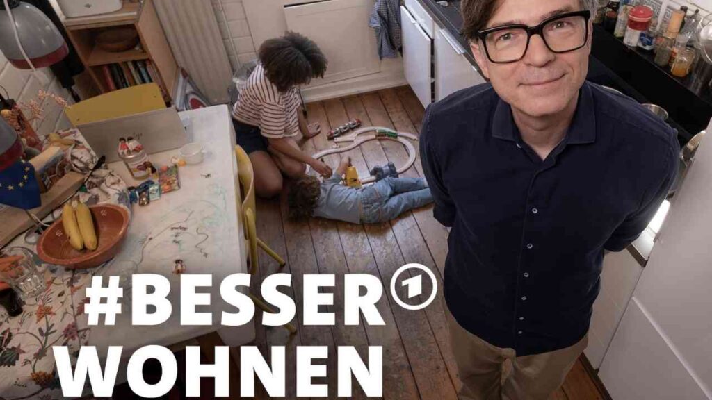 Ralph Caspers steht in einer Küche, während Kinder auf dem Boden spielen und Spielzeug verwenden.