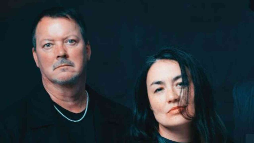 Porträt eines Mannes und einer Frau mit neutralem Ausdruck vor einem dunklen Hintergrund.