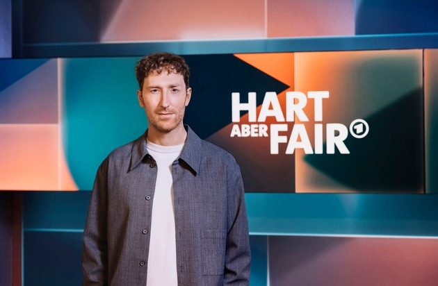 Mann steht vor einem Hintergrund mit dem Schriftzug 'HART ABER FAIR' in einem modernen Studio-Setting.