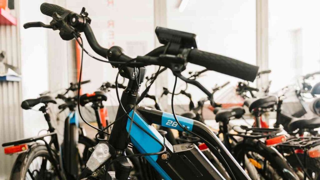 E-Bike mit blauer Rahmenfarbe und Display, im Vordergrund einer Fahrradwerkstatt mit weiteren Fahrrädern im Hintergrund.