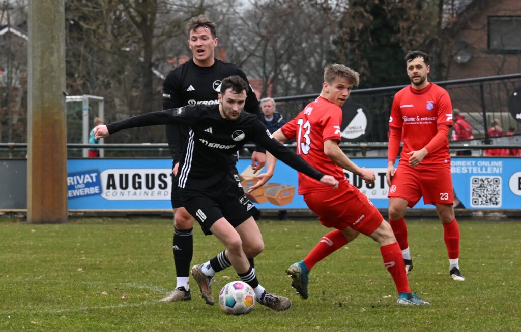 Fußballspieler in schwarzer und roter Ausrüstung während eines Spiels auf dem Platz.