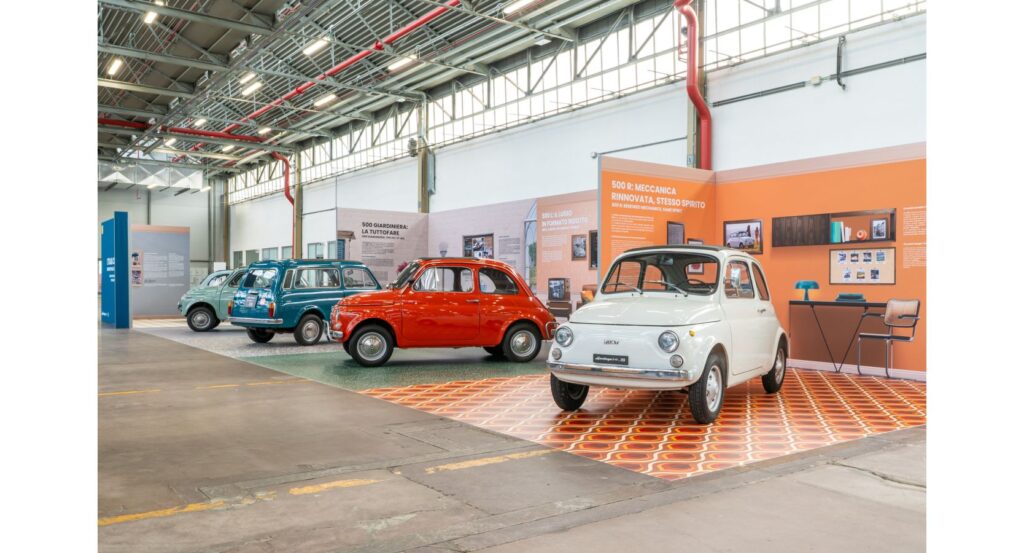 Drei klassische Autos in einer Ausstellungshalle, darunter ein rotes, ein blaues und ein weißes Modell.
